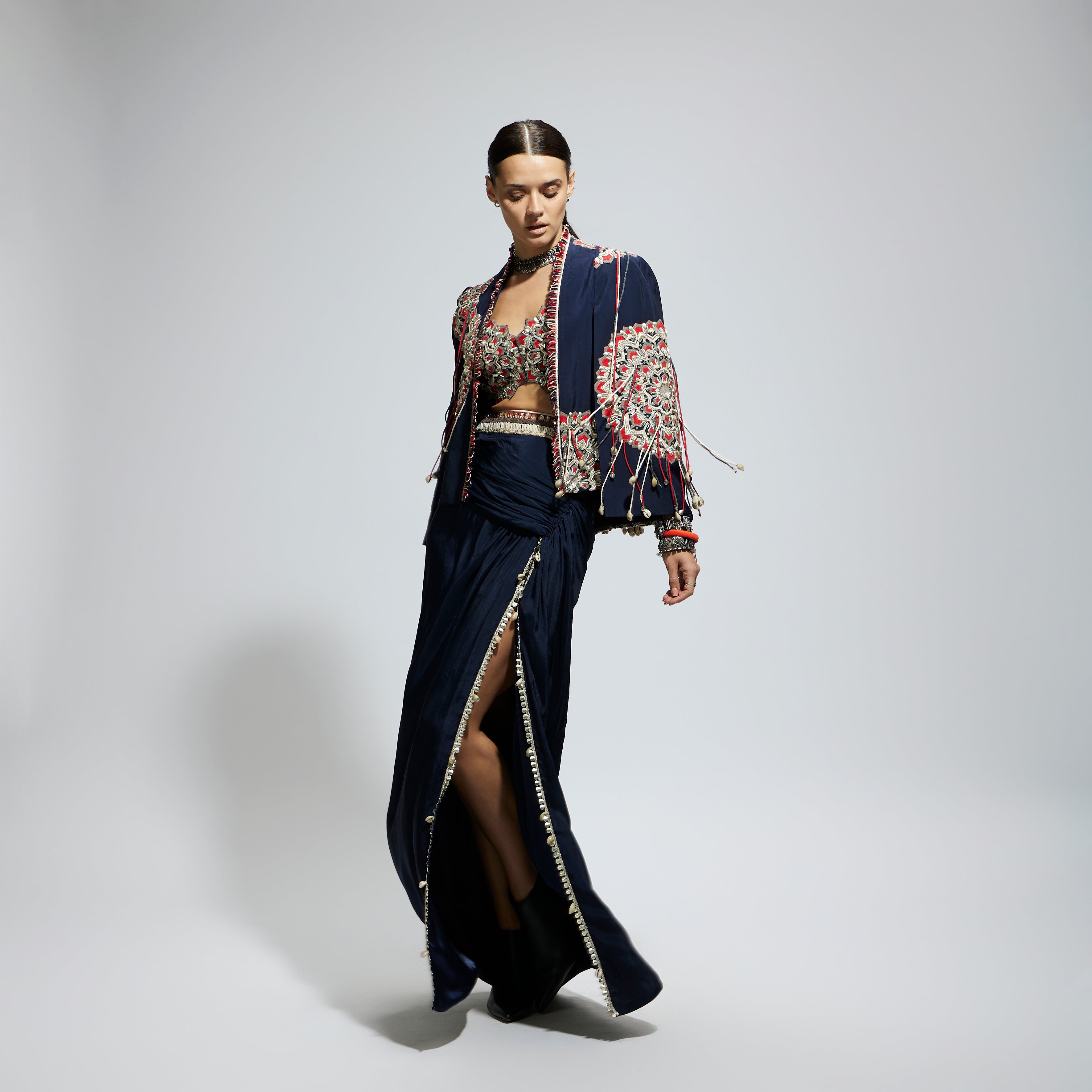 BLUE ASYMETRIC THREADWORK CAPE JACKET PAIRED WITH AN EMBELLISHED BUSTIER AND HIGH SLIT SKIRT