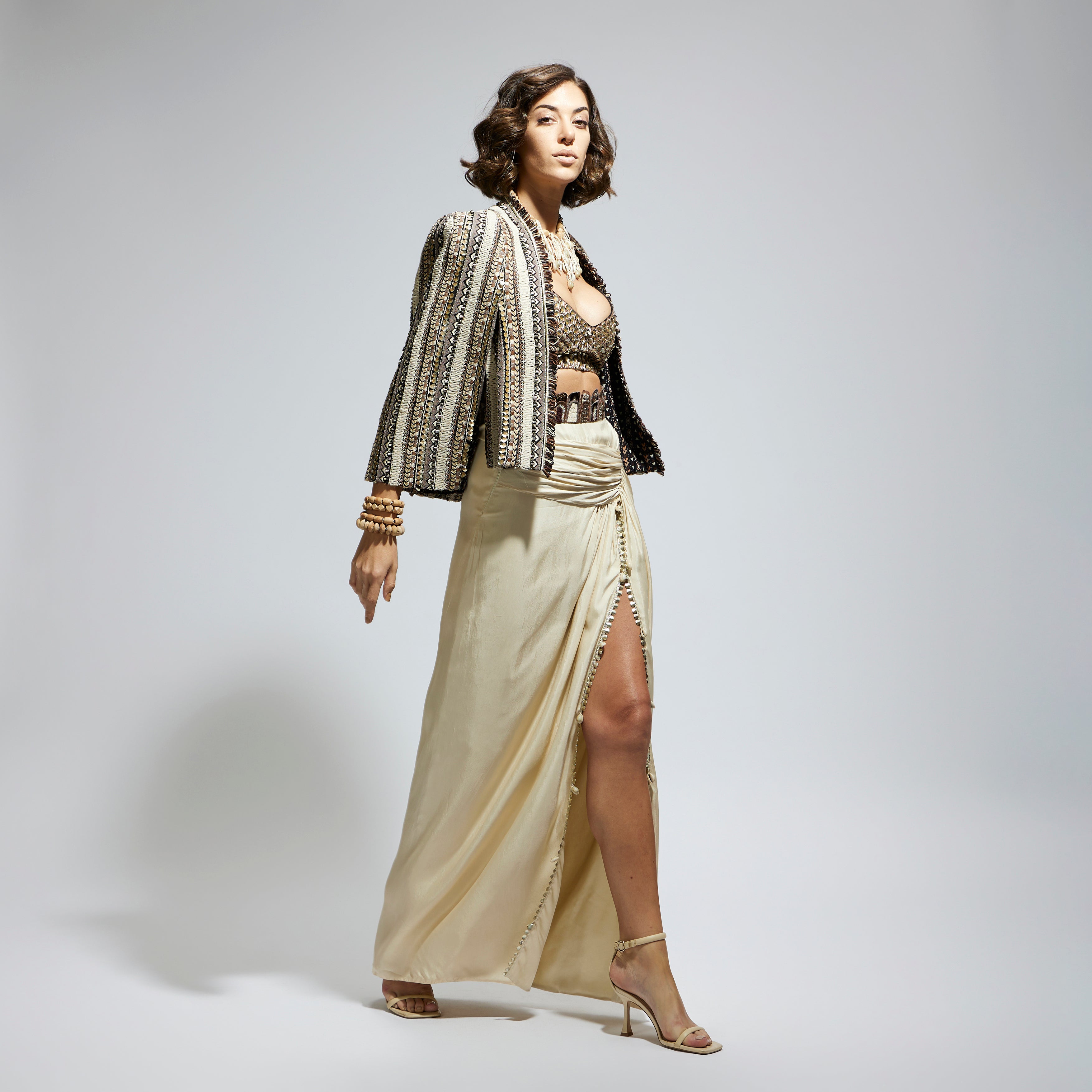 SAMSARA: EMBELLISHED & TEXTURED CAPE JACKET PAIRED WITH METALLIC SCALLOP BUSTIER AND IVORY HIGH SLIT SKIRT