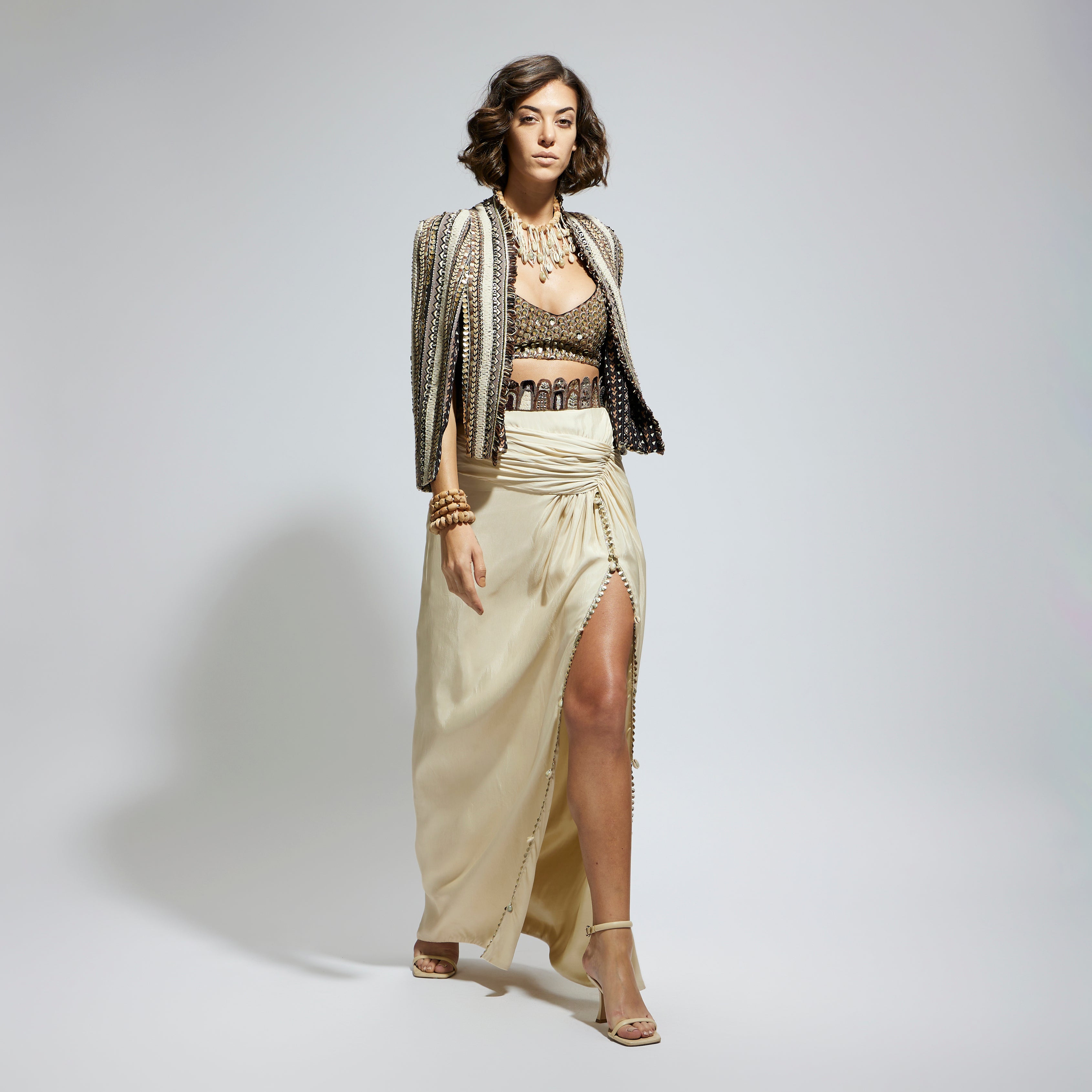 SAMSARA: EMBELLISHED & TEXTURED CAPE JACKET PAIRED WITH METALLIC SCALLOP BUSTIER AND IVORY HIGH SLIT SKIRT