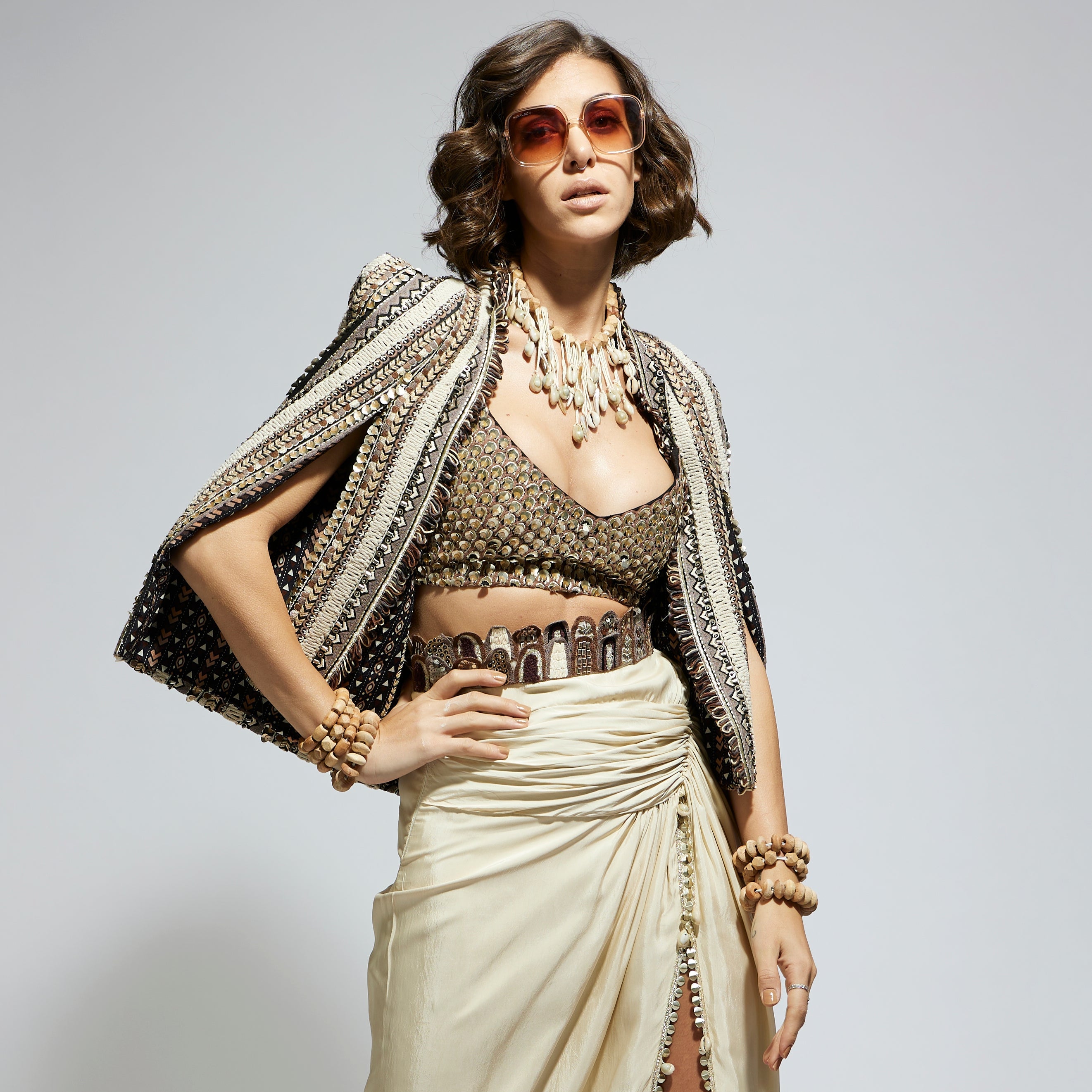 SAMSARA: EMBELLISHED & TEXTURED CAPE JACKET PAIRED WITH METALLIC SCALLOP BUSTIER AND IVORY HIGH SLIT SKIRT