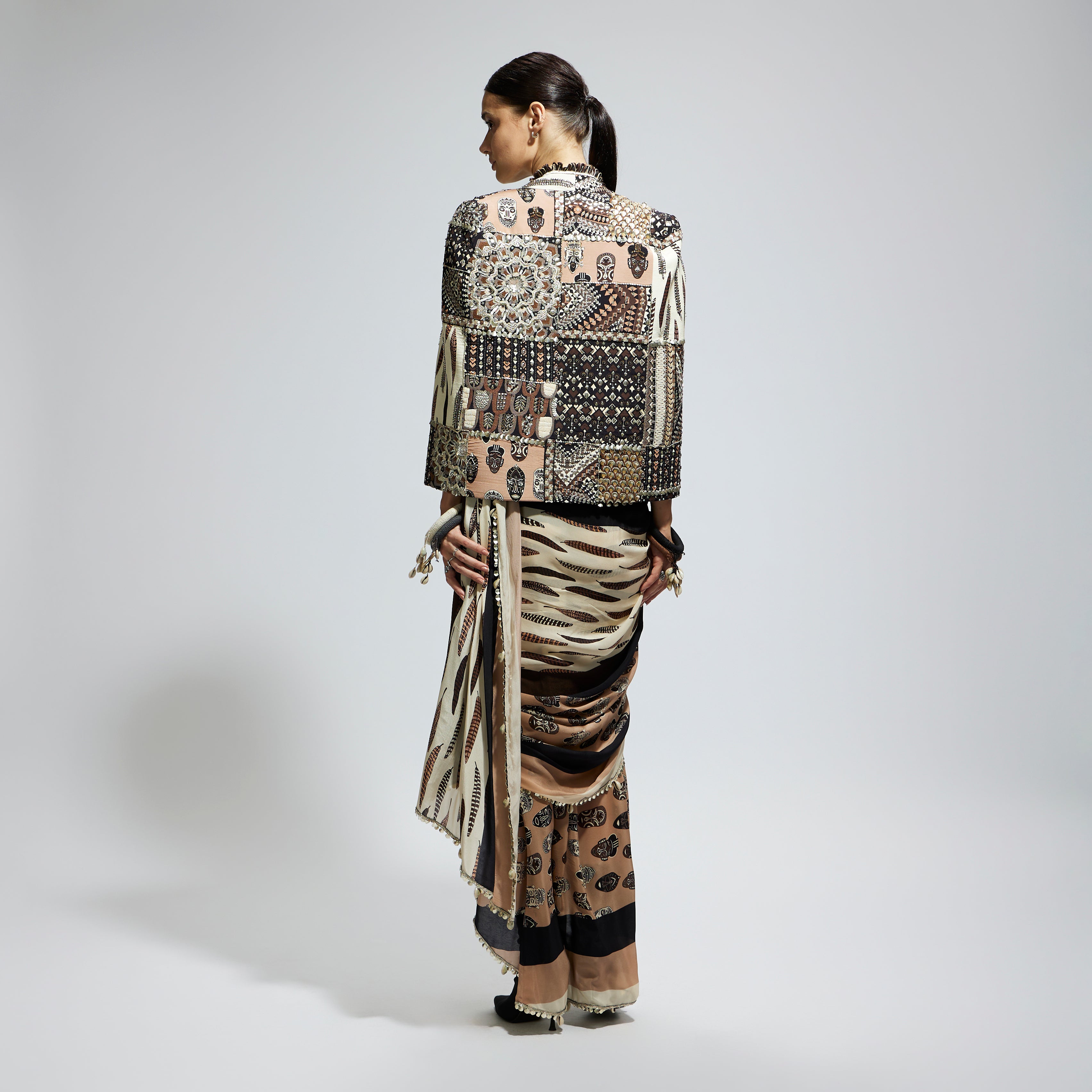 MASK AND FEATHER PRINT CASCADE SAREE PAIRED WITH METALLIC SCALLOP BUSTIER WITH PATCHWORK CAPE JACKET