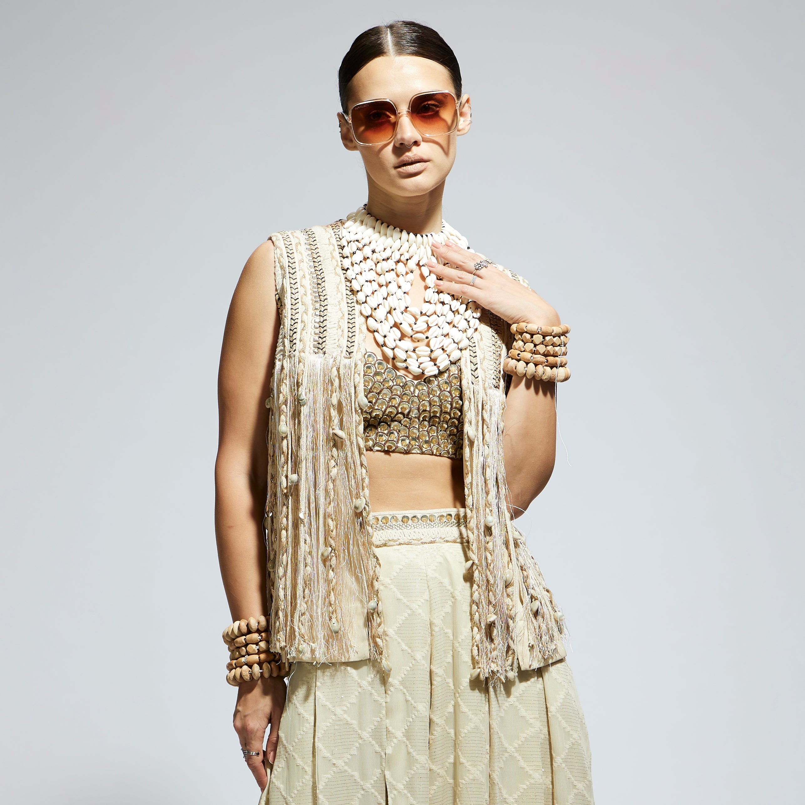 SAMSARA: IVORY THREADWORK FRINGE JACKET PAIRED WTH SCALLOP METALLIC BUSTIER AND IVORY AZTEC FLARED PANTS